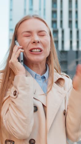 Caucasian mature businesswoman girl in coat arguing talking on smartphone on downtown city street