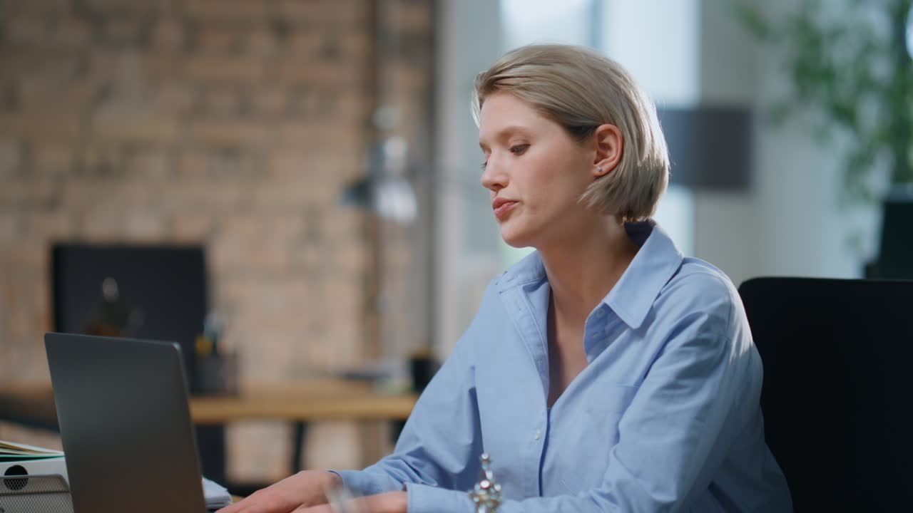 Erschöpfte Geschäftsfrau schließt Laptop in leerem modernen Büro (Nahaufnahme).