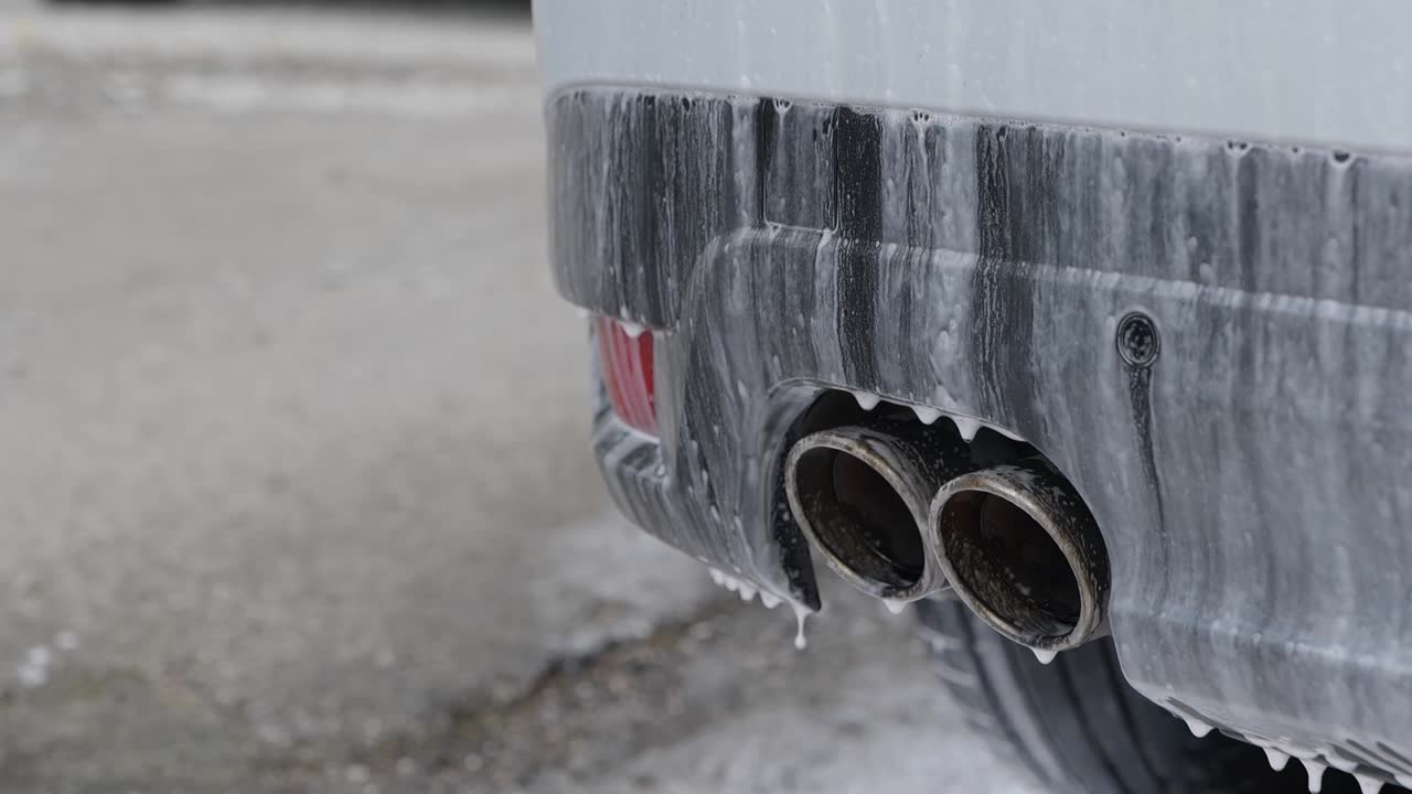 Close up of snow foam cleaning solution soaking on rear bumper and exhaust