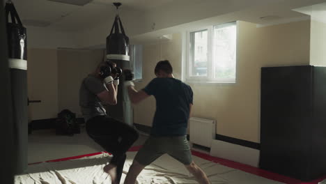 los kickboxers luchan en sparring amistoso en un club deportivo. los jóvenes maestros de artes marciales ejercitan ataques y bloques en un gimnasio vacío. los deportistas entrenan en combate.