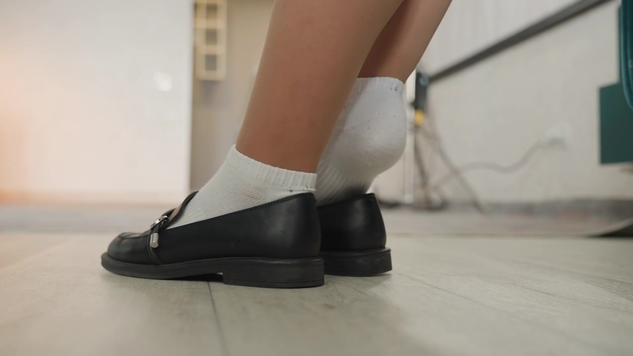 Mulher caucasiana testando sapatos após limpar a casa, close-up de pé com meia pisando em piso recém-limpo com mocassins pretos por perto, proprietária inspecionando o brilho, movimento prático e cuidadoso em ambiente claro.