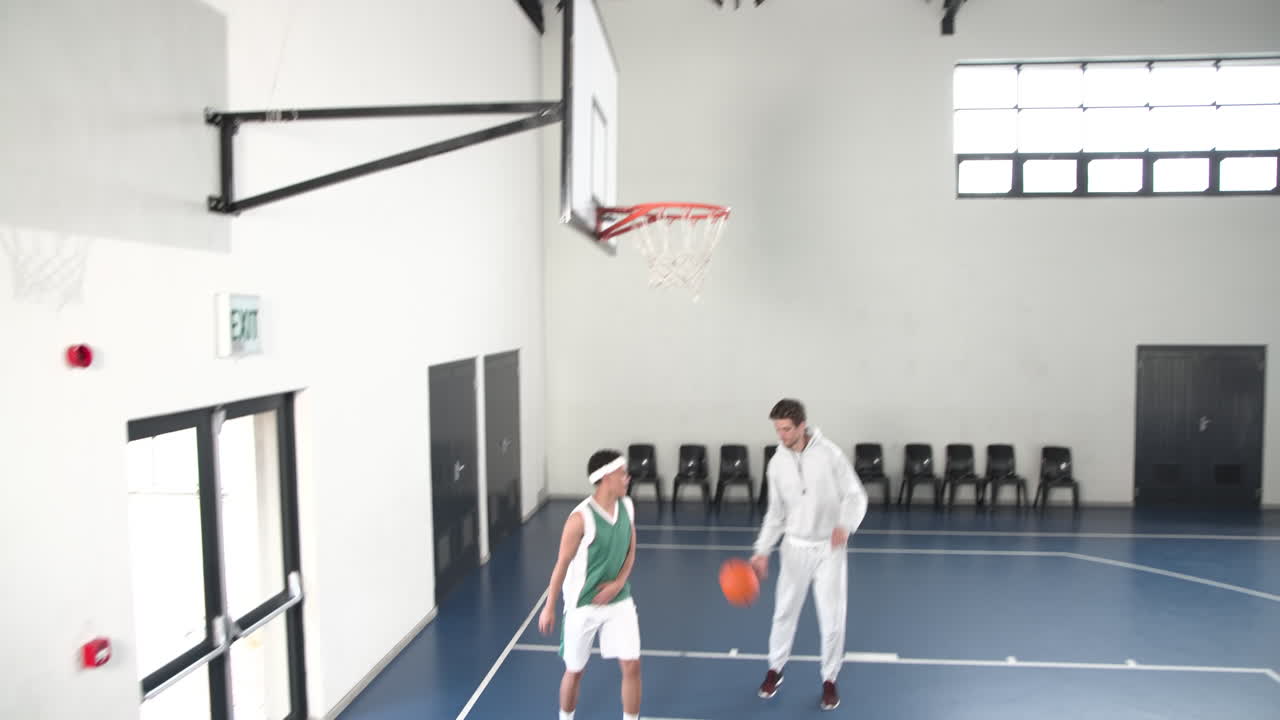 Coach observing basketball player practicing dribbling skills on indoor court