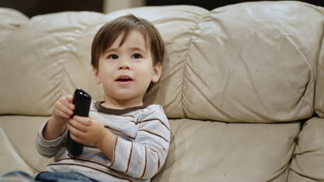 asian two years old kid watches tv, holds a remote control in his hands