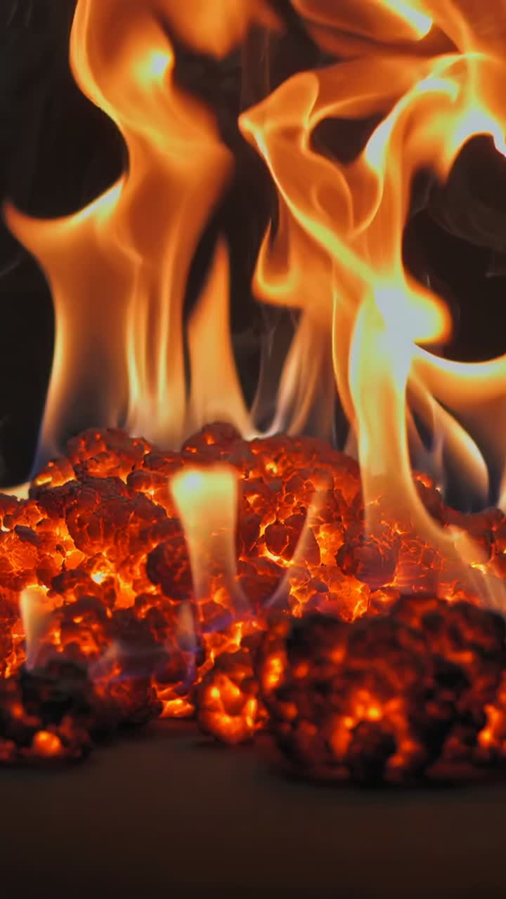 Vertical video: Flickering flames and glowing coals shifting with draft, consuming embers in hearth