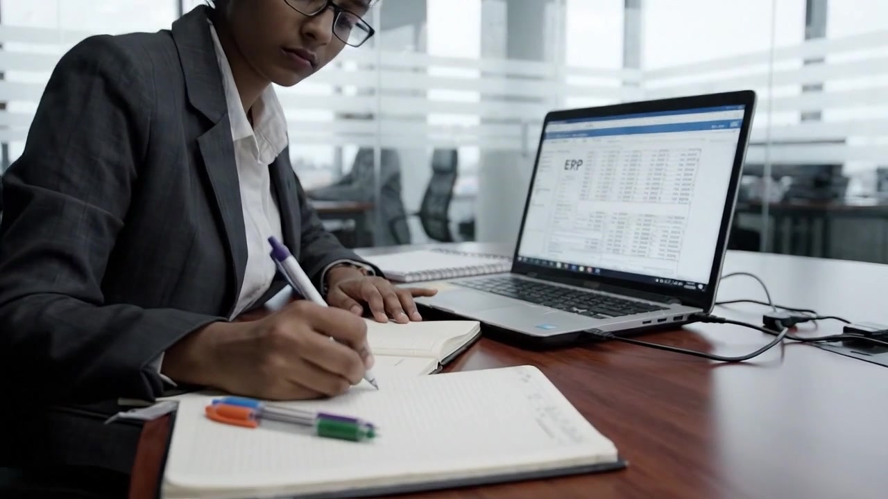 Profesional yang Fokus Bekerja di Lingkungan Kantor Modern, Sibuk dengan Laptop, Mencatat, Dikelilingi Rekan Kerja, Menekankan Produktivitas dan Kolaborasi