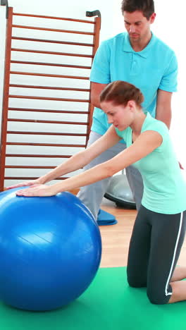 trainer helping his client stretch her back with exercise ball