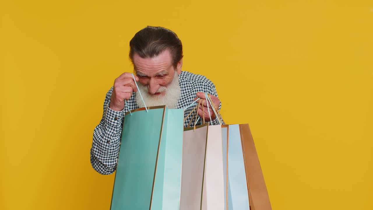 Happy senior old man shows shopping bags advertising discounts amazed with low prices holidays sale