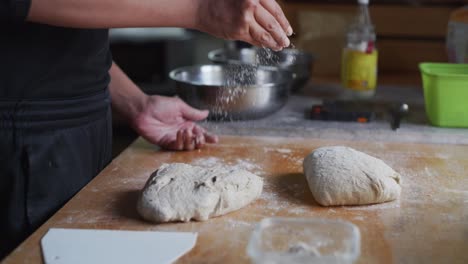 dry white flour sprinkled over wooden tabletop next to freshly risen dough, filmed as medium closeup slow motion shot