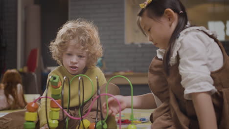 little girl and little boy playing with wooden pieces that move in a wire in classroom in a montessori school 1