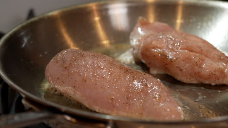 boneless, skinless chicken breasts frying in a skillet - slow pan right