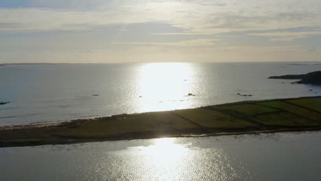 ascending aerial of ardmore island with the sun’s reflection stretching to the horizon.