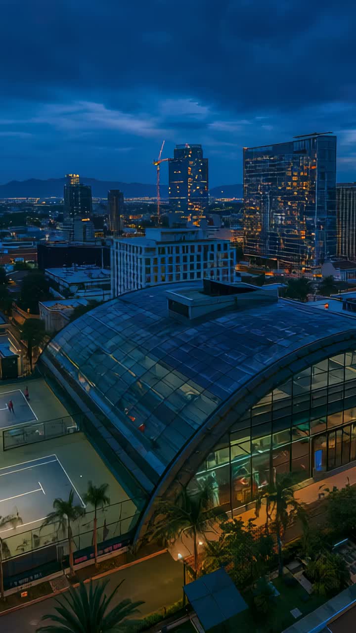 Vertical video: Tilting drone over downtown at dusk, showing arched glass roof and tennis courts