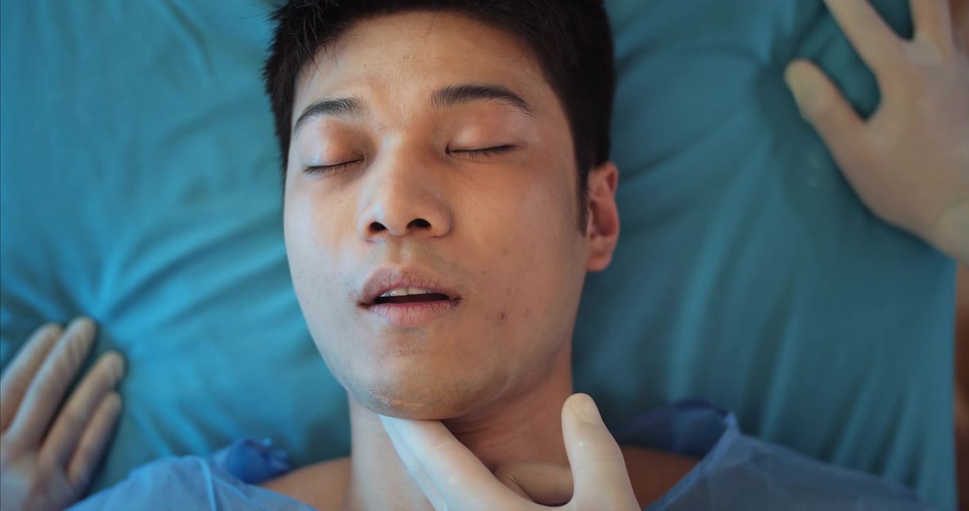 Medico che controlla il polso di un uomo asiatico incosciente in un letto d'ospedale