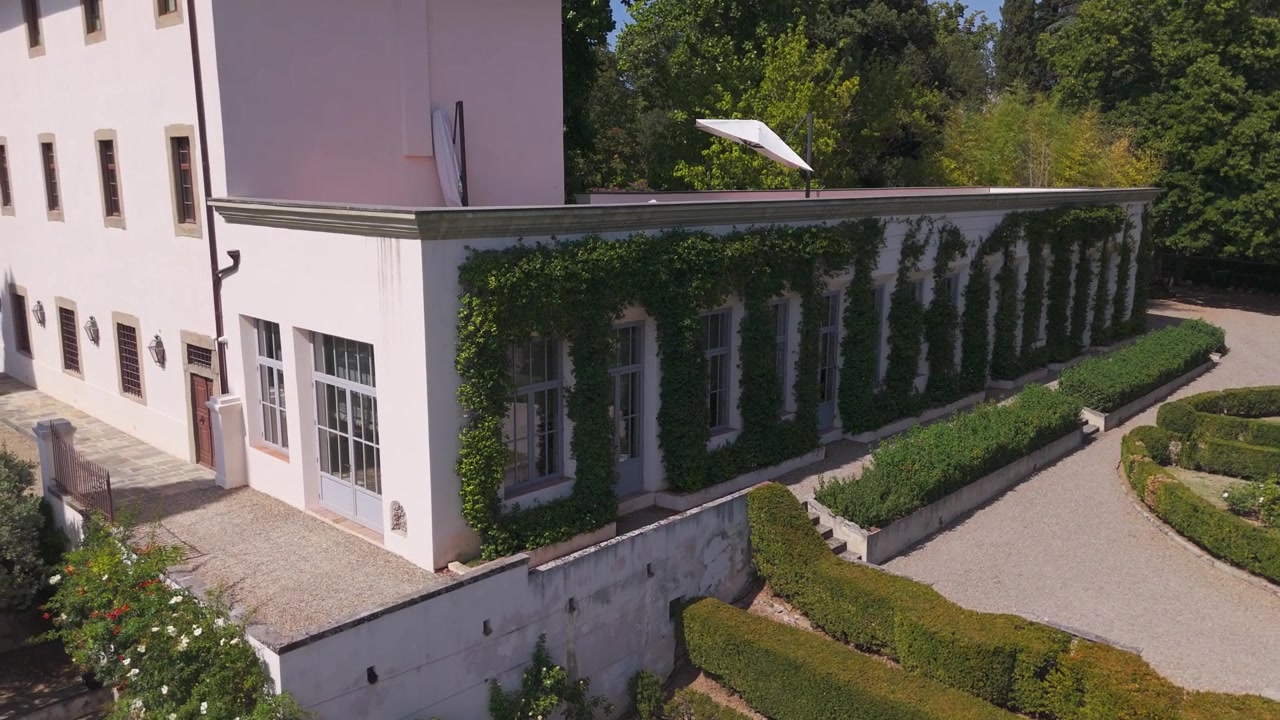 Vue de drone d'une villa à la façade recouverte de lierre, avec un jardin impeccablement entretenu et des allées de gravier.