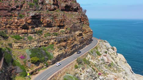 an aerial shot of cars traveling on a dangerous narrow mountain road along the ocean chapmans peak road near cape town south africa