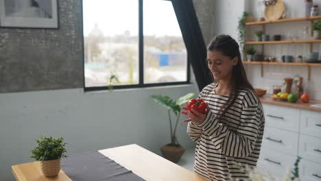 young woman playing with red bell pepper in kitchen