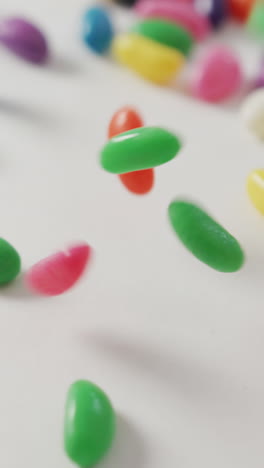 video of close up of multi coloured sweets falling over white background