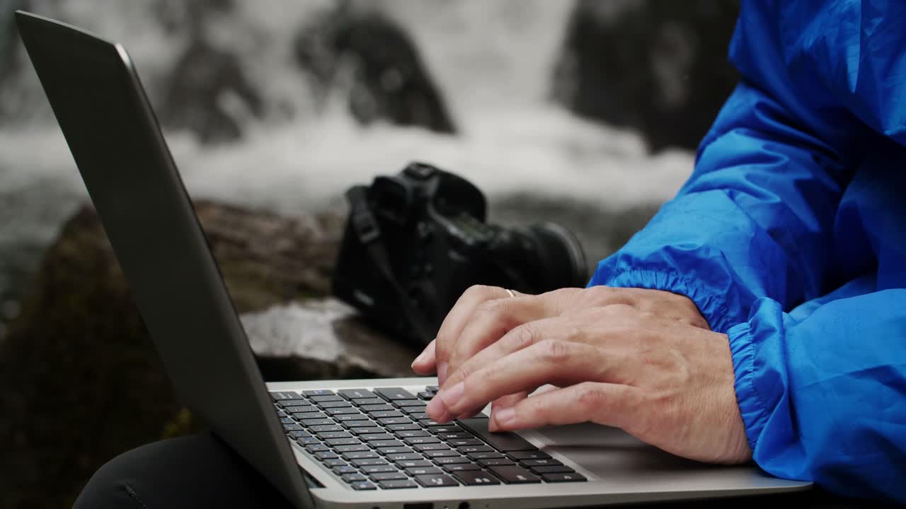 Person working on a laptop by a waterfall