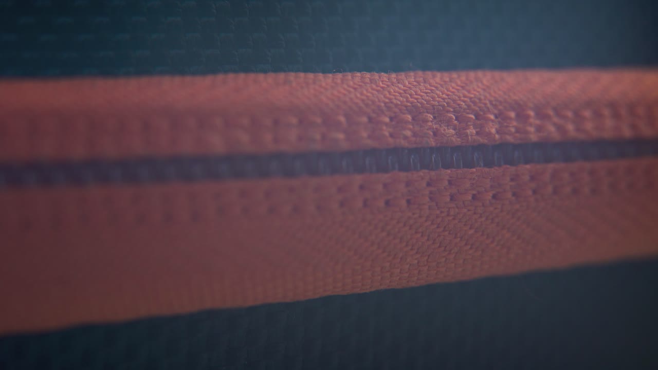 단단한 케이스 지퍼가 천천히 열리는 매크로 클로즈업, 오렌지색 레크처, 금속 지퍼, 블랙 박스, 사진 장비, 전문 스튜디오 조명, 정적 4k 비디오