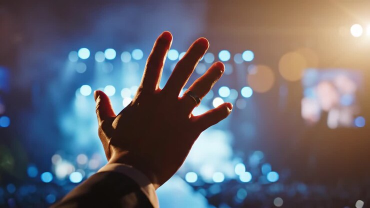 Mano che si allunga verso le luci del palco durante un concerto
