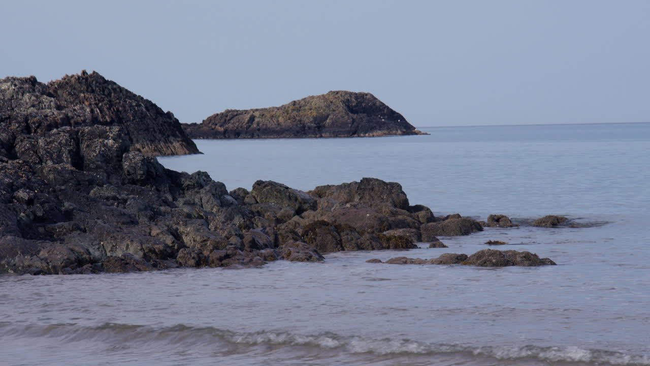 Billede af små bølger, der bryder mod klipperne ved Llanddwyn Beach og Newborough National Nature Reserve