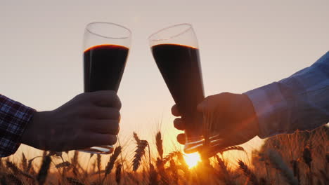 two male hands clink glasses of beer at sunset