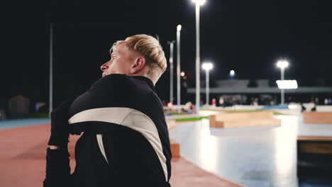 sportive blond man doing stretching exercises before training in the park at night 4