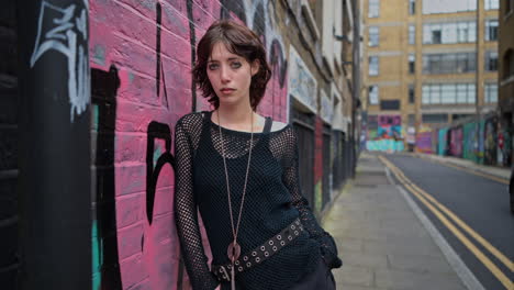 retrato de moda al aire libre de una mujer joven de estilo alternativo apoyándose en una pared cubierta de graffiti en la calle de la ciudad de londres, reino unido, en tiempo real.