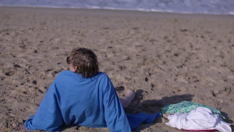 Middle-aged-white-woman-sitting-on-beach-overlooking-Pacific-Ocean-in-Venice-Beach,-California-in-slow-motion