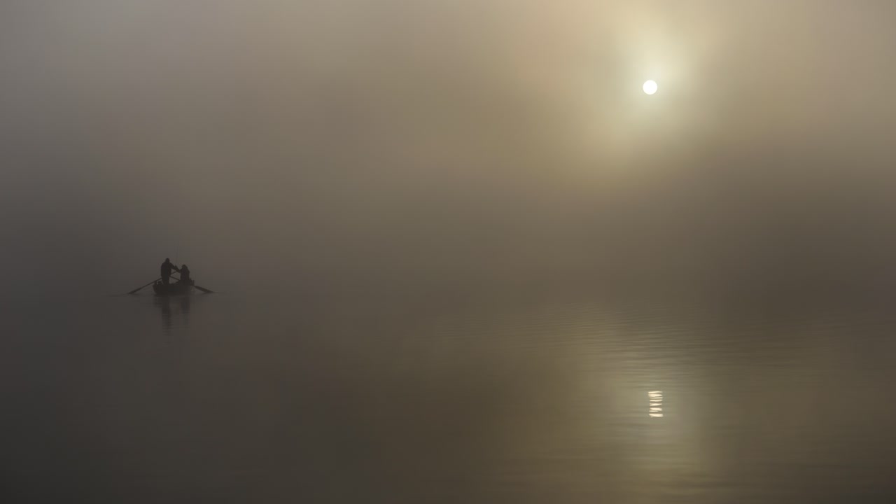सुबह-सुबह, दो मछुआरे, जिनकी परछाई दिख रही है, कोहरे और सूर्योदय में झील पर हैं और कोहरे में चप्पू चला रहे हैं। यह एक रहस्यमय और शांतिपूर्ण वातावरण है। पानी शांत है