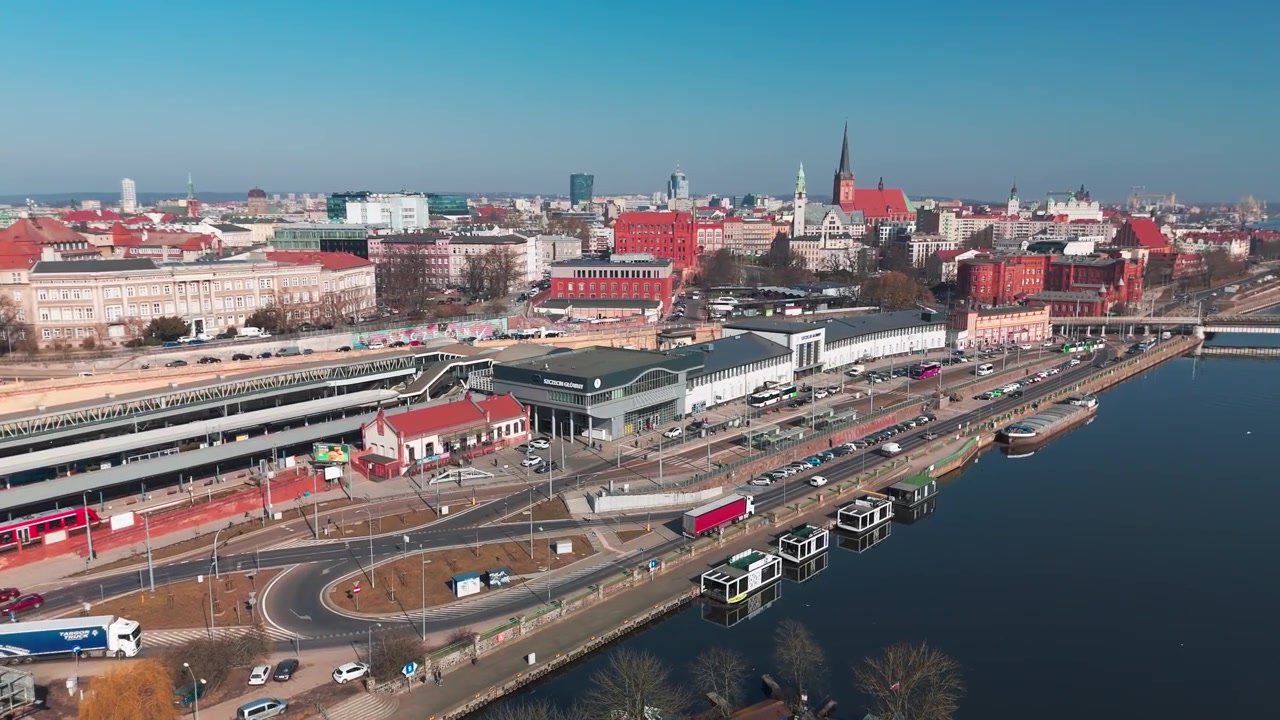 En vidvinkelbild med drönare som visar Szczecin Glowny tågstation, stadssiluetten med historiska kyrkor och floden Odra en klar solig dag.
