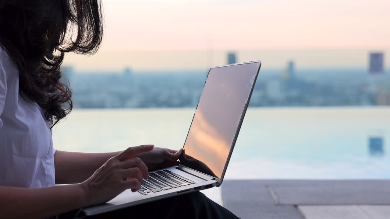 vista recortada de una mujer escribiendo en el teclado mientras está sentada en su lugar de trabajo en un lugar acogedor y relajante en el hermoso cielo del atardecer del verano.