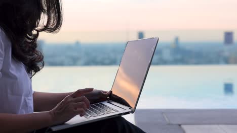 cropped view of woman  typing on keyboard while sitting at her working place in cozy, relaxing in summer beautiful sunset sky.