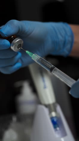 in a beauty clinic, a gloved professional draws liquid from a vial into a syringe - close up