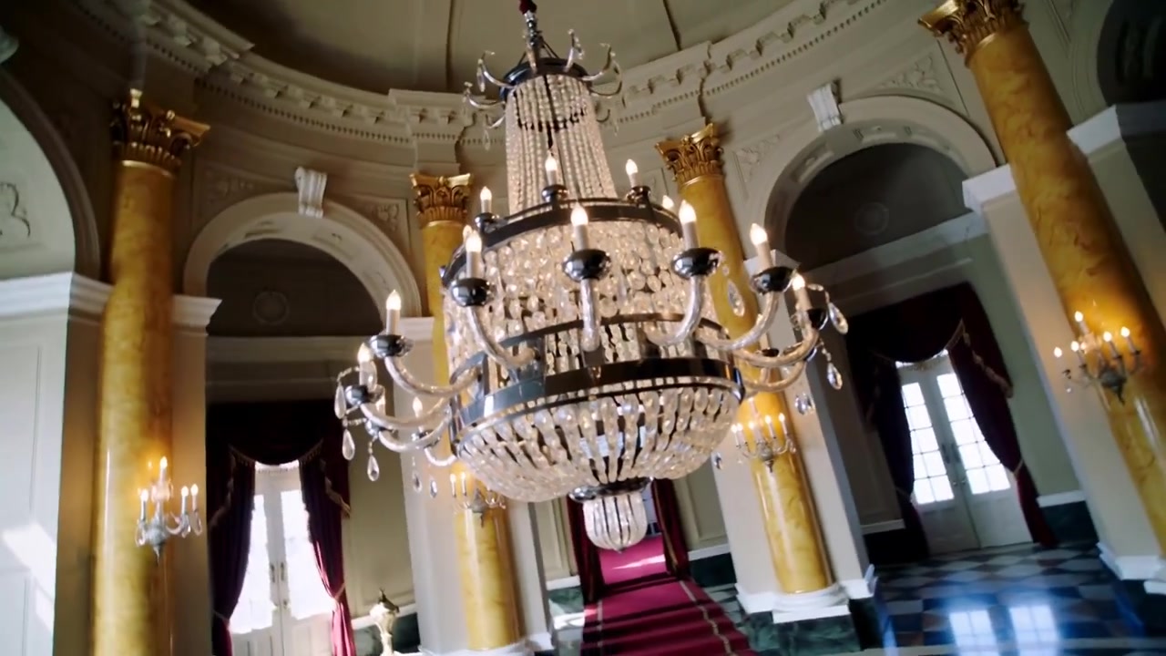 Telecamera che si inclina rivelando un lampadario di cristallo a più livelli in una grande sala circolare per mostrare l'arredamento ornato.
