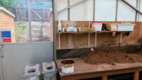 A stationary camera captures a potting bench in a greenhouse as trays, soil, and gardening supplies are arranged under natural daylight, revealing workspace organization