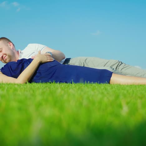 young husband with his pregnant wife relaxing in the park together lie on the green grass