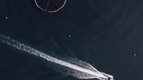 bird's eye view drone shot of the wake of a fishing boat at a fish farm