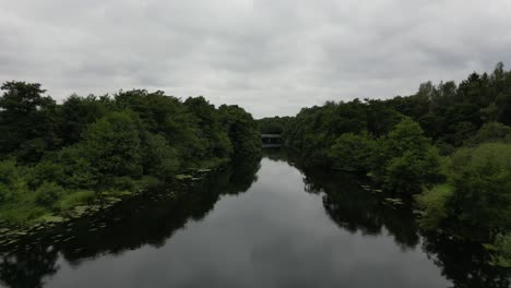 Drone-recording-of-the-Gudenå-River,-where-the-drone-flies-over-and-along-the-stream-on-its-way-to-a-small-bridge