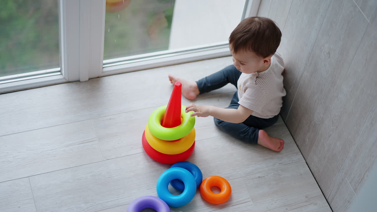 Lovely Caucasian child puts colorful rings on the base. Baby boy playing with toy pyramid. Top view.