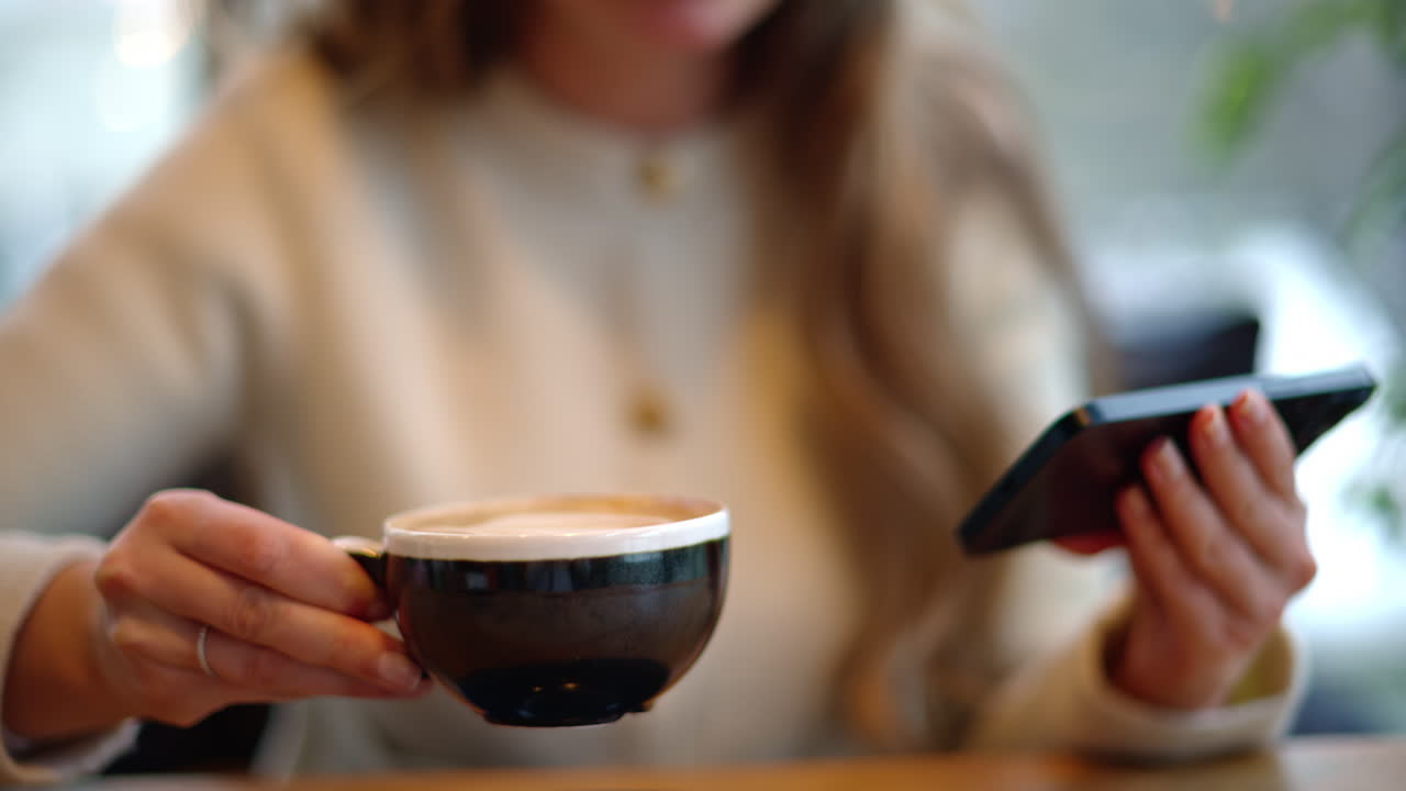 Woman drinking latte coffee while watching content on smartphone
