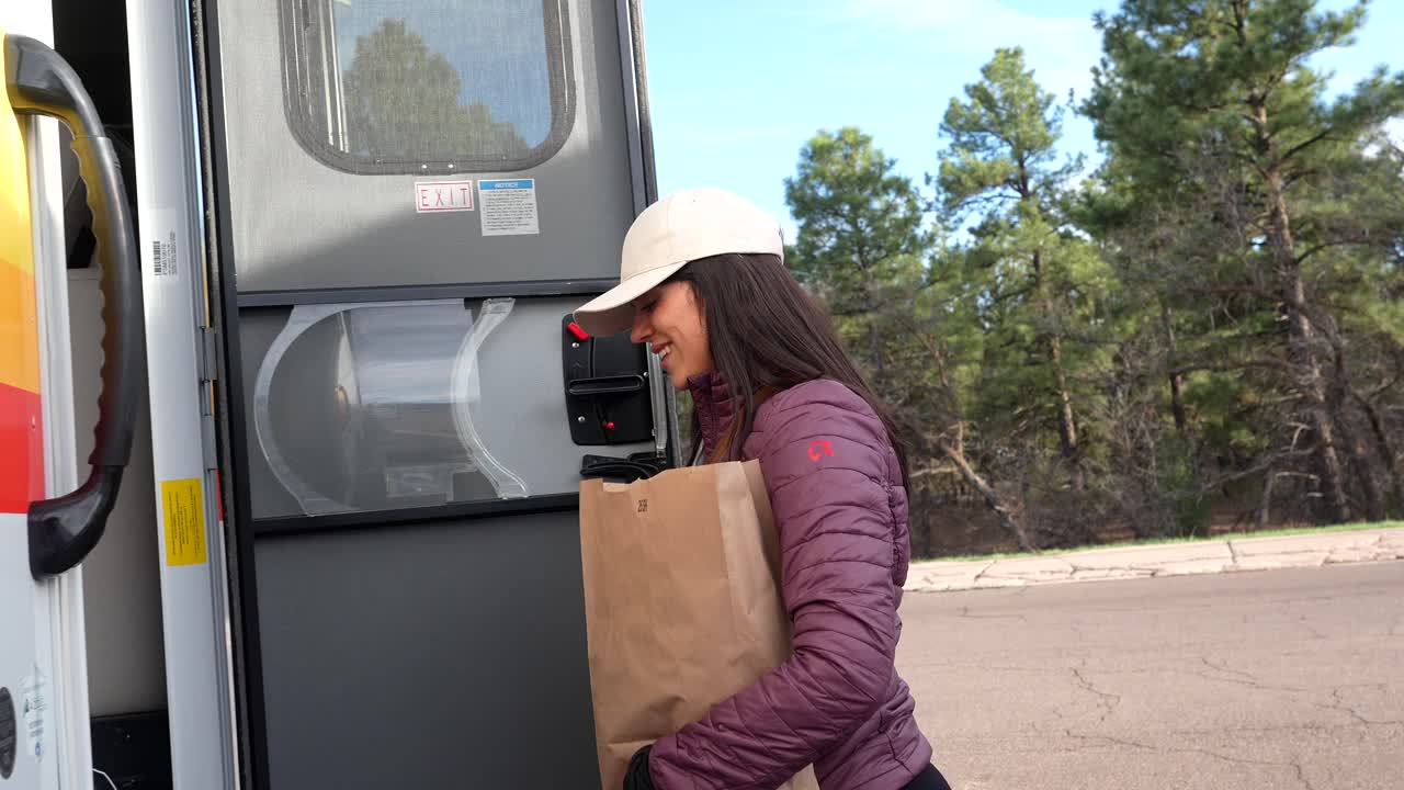 Joven feliz entrando en una autocaravana con una bolsa de papel al aire libre