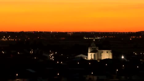 Foco-Aéreo-Del-Edificio-Iluminado-Por-La-Noche-Con-Cielo-Naranja-Al-Atardecer