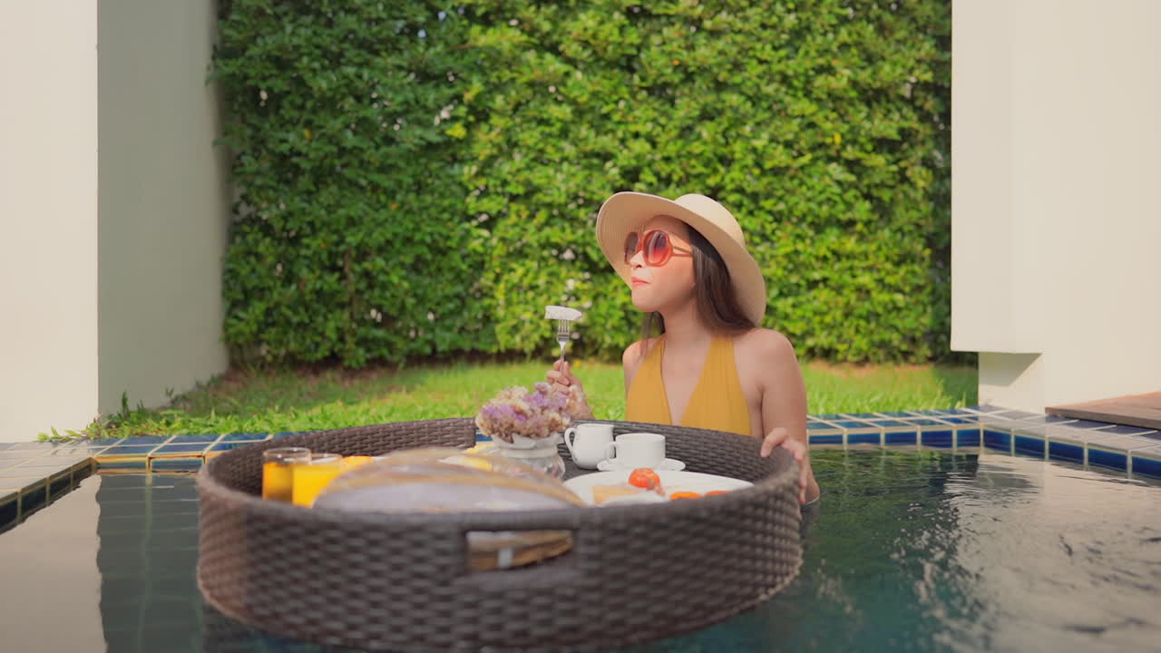 A woman in a resort pool rotates a floating plater of food before taking a bit of her food