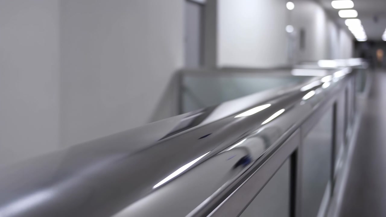 Vista ravvicinata di un'elegante rotaia metallica all'interno di uno spazio industriale interno, con bordi riflettenti, illuminazione soffusa dall'alto e forti linee prospettiche che enfatizzano superfici lisce e un design strutturato.