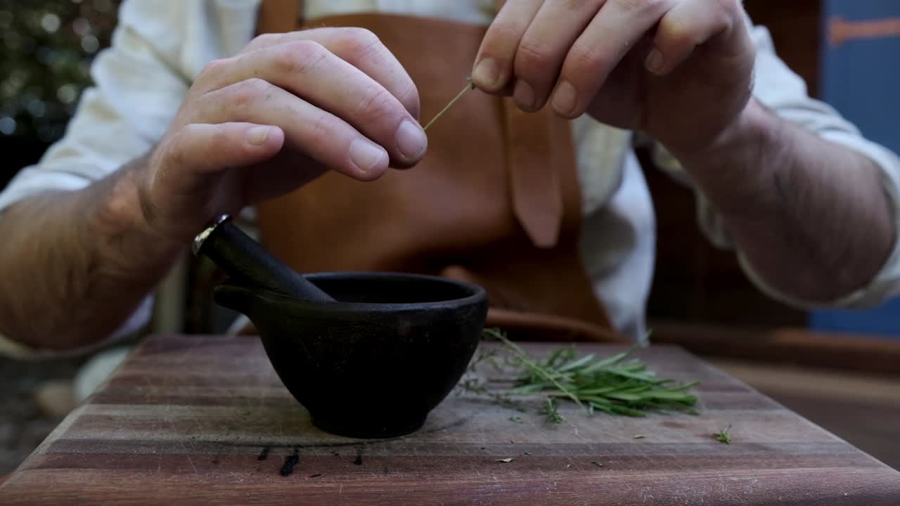 hombre preparando hierbas para cocinar con una maja y un mortero