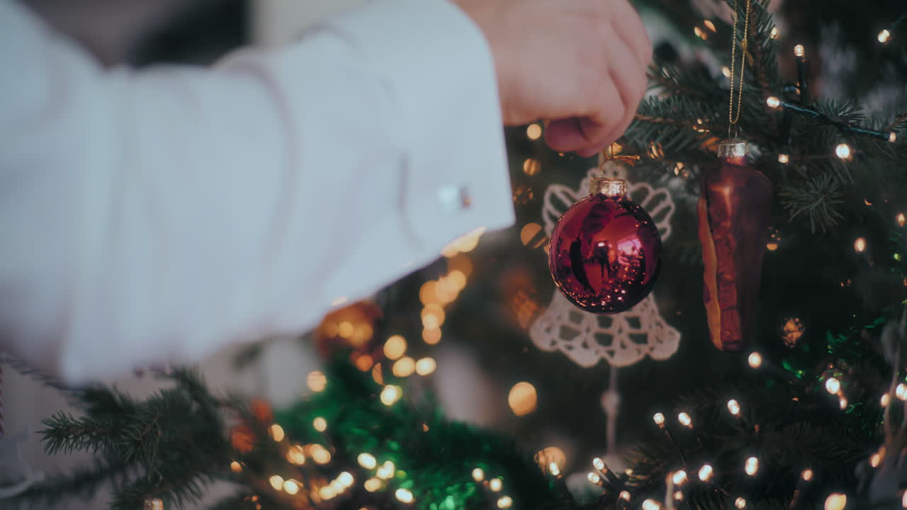 la mano colgando una joya roja y brillante en el árbol de navidad en casa