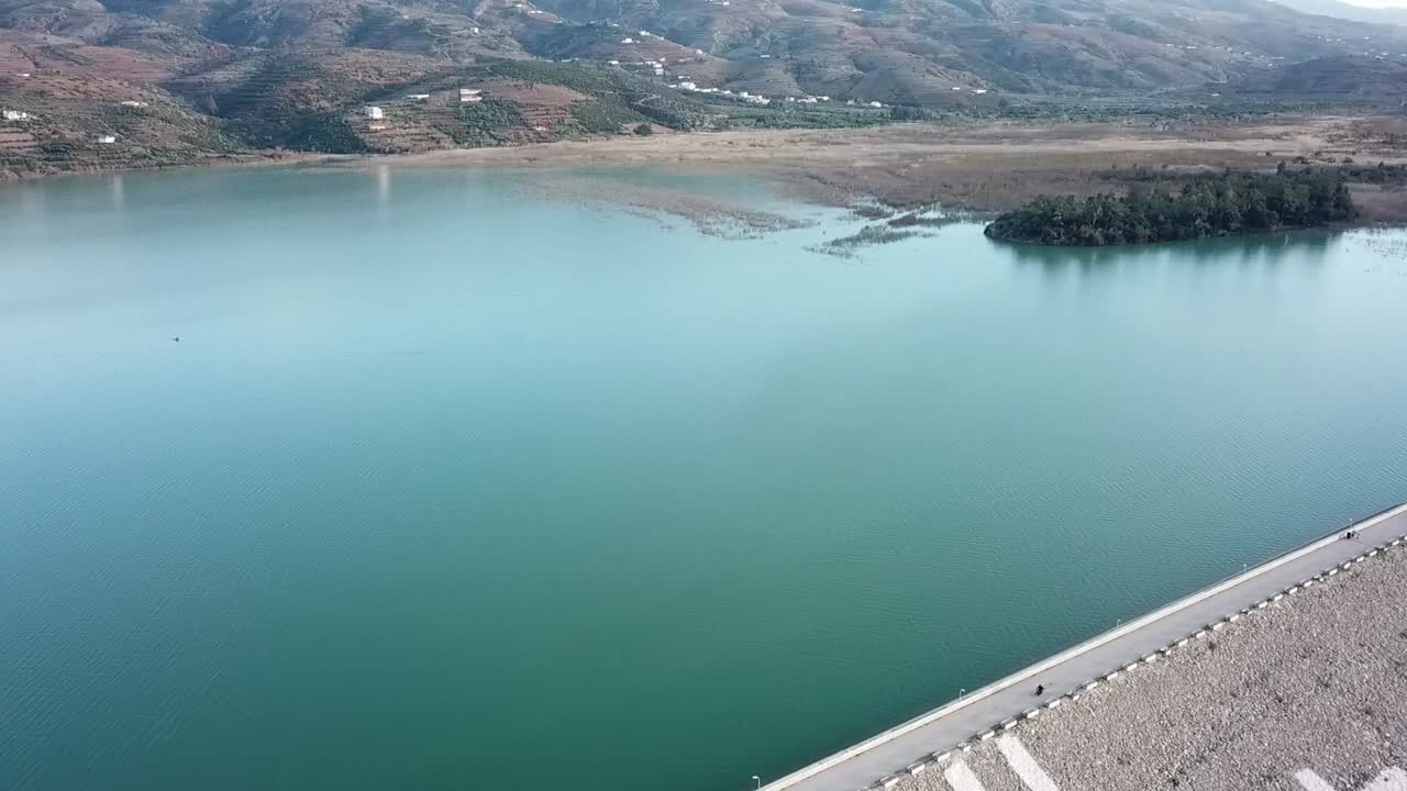 Drone footage showing a large water dam reservoir surrounded by the rugged terrain of the Rif Mountains. Hydraulic infrastructure in Morocco