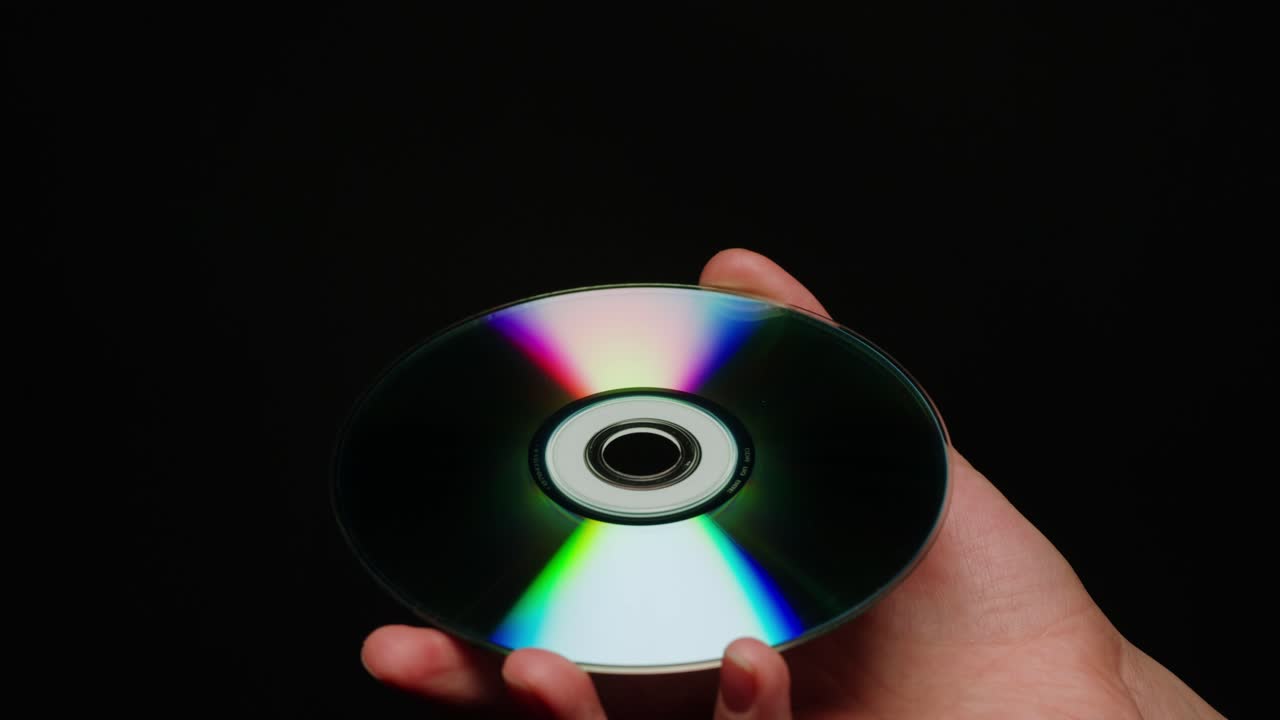 CD disk in hands on black background close-up. Old vintage disks for DVD player or computer. Music recorder, playing retro computer games.