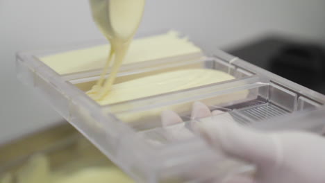 hacer una barra de chocolate blanco, verter chocolate blanco en un molde de plástico con un cucharón en confitería